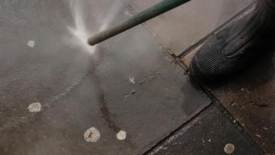 A street cleaner hoses chewing gum from a pavement