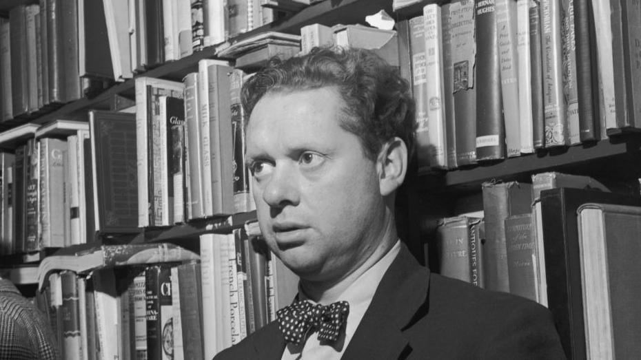 A picture of Welsh author Dylan Thomas standing in front of a bookshelf at the Gotham Book Shop during a reception held in his honour in New York City