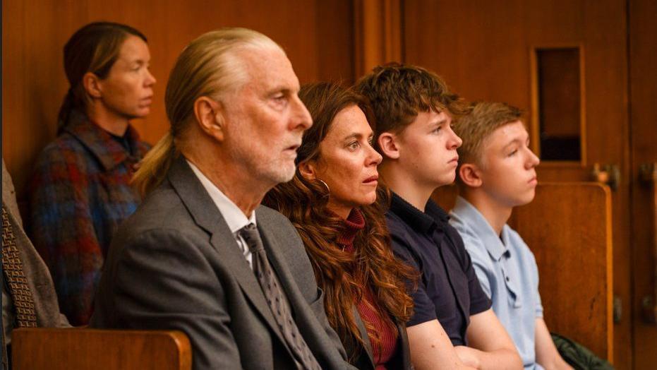 This candid still from the drama shows several of the character sitting in a court room. They are all staring directly ahead.