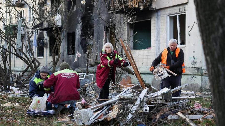 Workers clean up debris, outside an apartment building damaged during an overnight Russian drone and missile strike, amid Russia's attack on Ukraine, in Kyiv