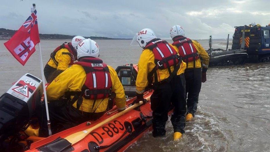 Lifeboat crew push out a speedboat from shallow water with another sat by the engine 