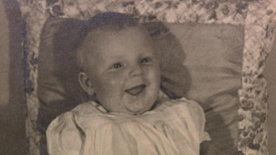 Michael Hamson as a baby. He appears to be a in a cot wearing white clothing with a big smile. 