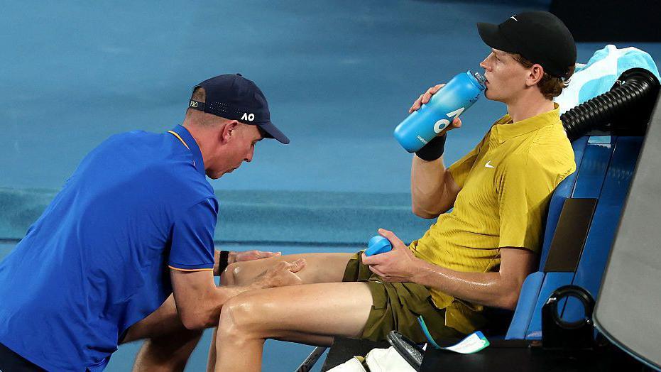 Jannik Sinner (right) receives treatment on his right leg