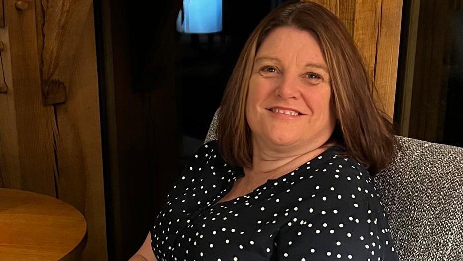 Rachael Evans, CEO of Charcot. She is smiling, she has a brown bob and is wearing a black dress with white polka dots.