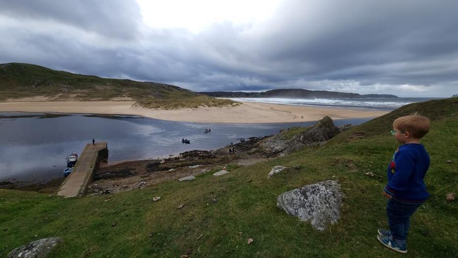 A boy dressed in blue looks down on Bettyhill pier 