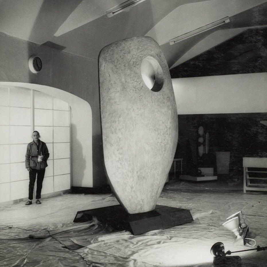 A black and white photograph showing Barbara Hepworth standing to the left of a tall upright plaster prototype for Single Form (Memorial) in the Palais de Danse in March 1962 