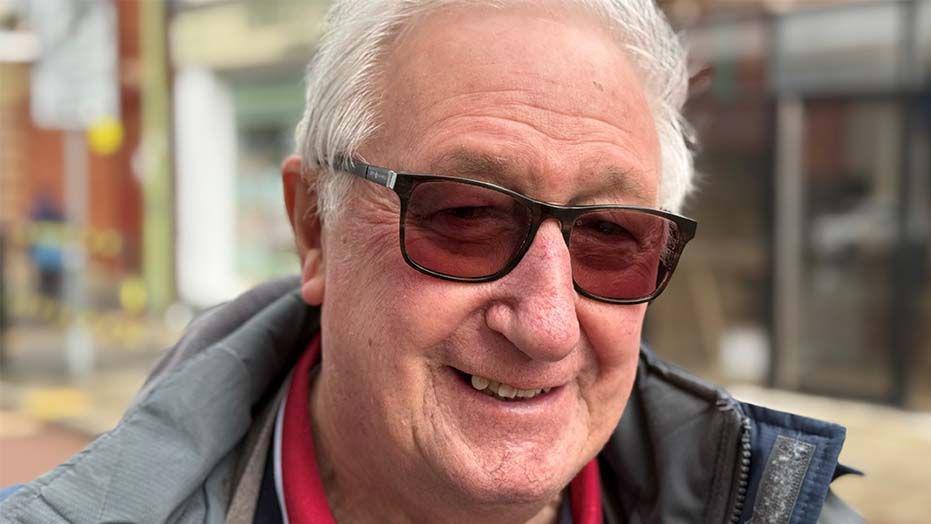 Head shot of Joe Pownall, he is smiling, has short, white hair and is wearing sunglasses