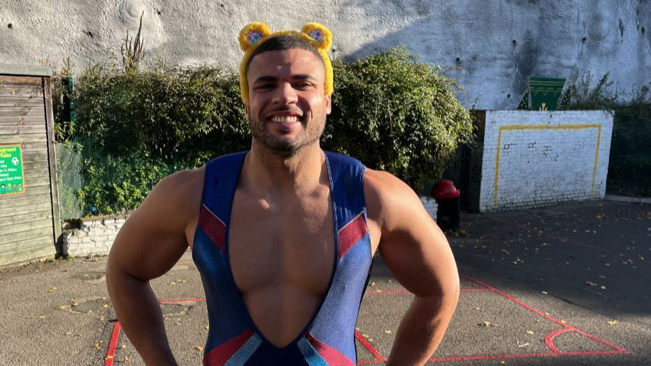 Gladiator Steel in a blue lycra sleeveless vest with hands on hips and wearing Pudsey ears