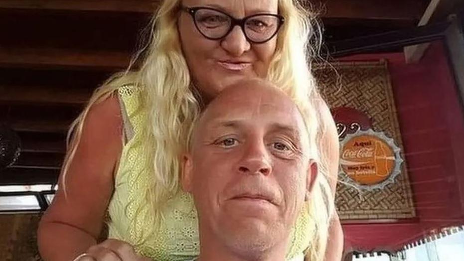 Woman with long blond hair and black glasses and yellow sleeveless top stands behind her partner Tony Johnson. The woman's name has not been disclosed by police.