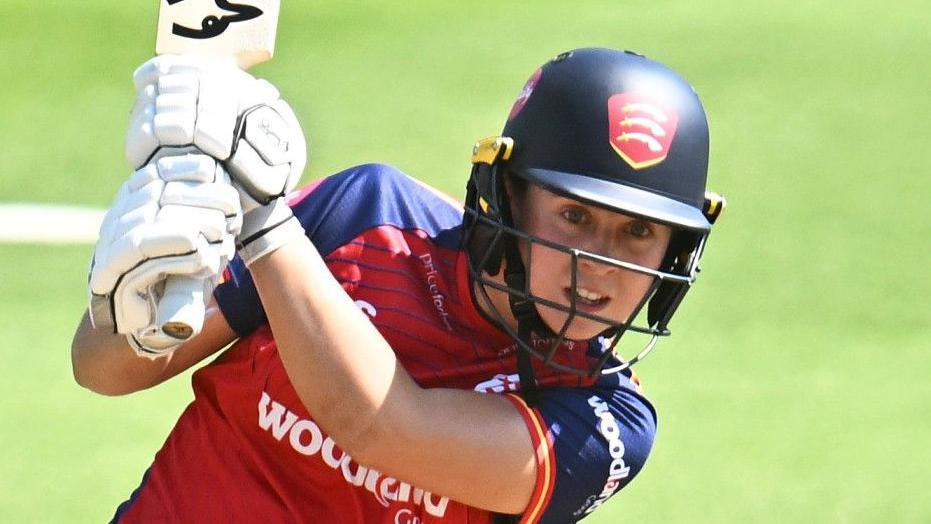 Jodi Grewcock wearing an Essex Cricket jersey and helmet swings her bat during a match.