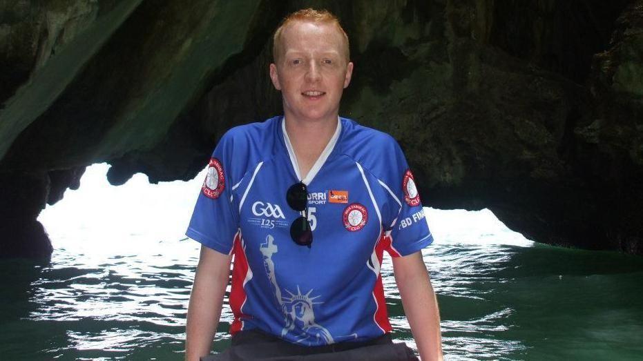 Kevin Bell pictured in a blue GAA top, in front of water in a cave with black sunglasses on his top