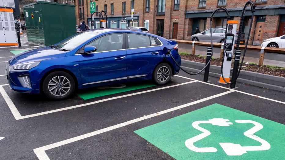 Blue car in a car park and being charged at a public charging point