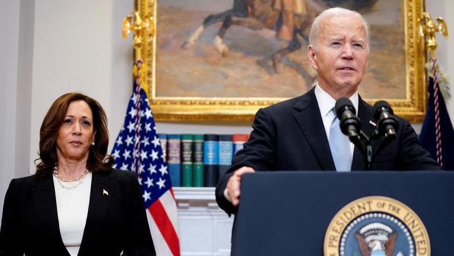 Joe Biden standing at a podium in a room in the White House making an address - Kamala Harris is standing behind him