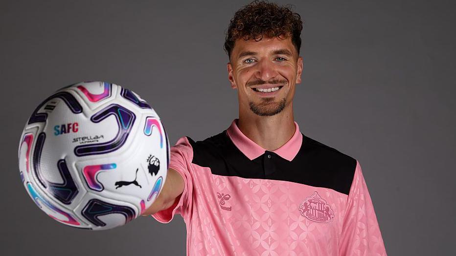 Thomas Meunier holds a ball outstretched in his right hand. He is wearing a pink Sunderland jersey