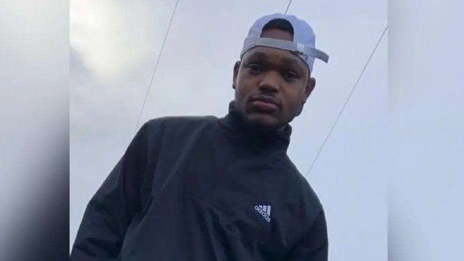 Lazarus Mokono, a young man wearing a black Adidas tracksuit and white baseball cap back to front, against the backdrop of a cloudy sky.