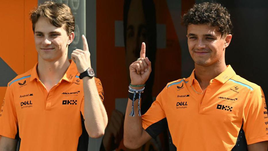 McLaren's Oscar Piastri and Lando Norris clasp up their scale fingers while stood adjacent to each different and smiling