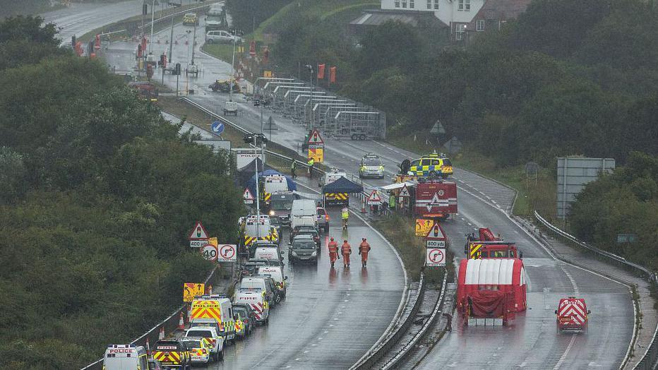 Both carriageways of a motorway are shut off with a large number of emergency vehicles in the road.