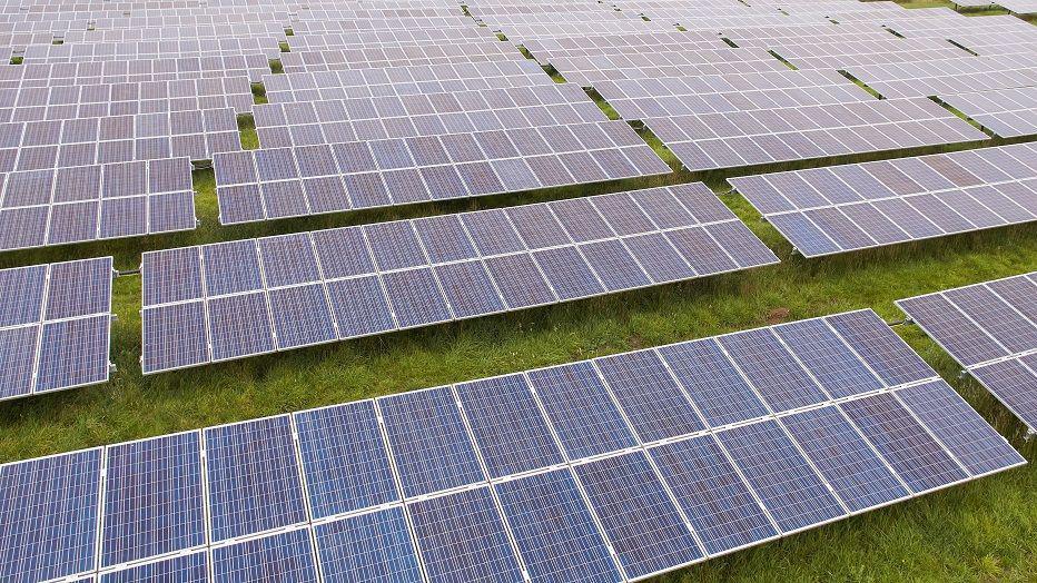An aerial photo of a solar farm which is made up of rows of solar panels on top of a patch of grass.