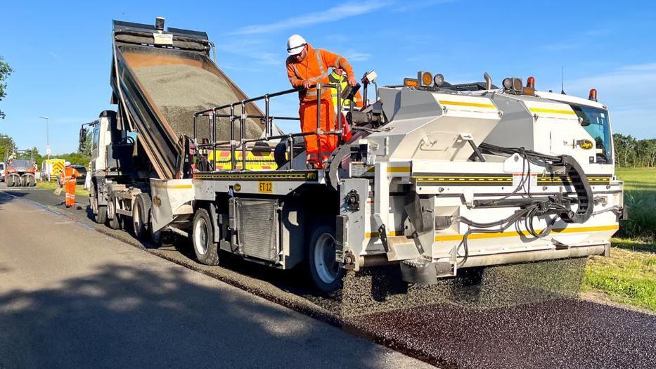 Worker in orange on top of truck as surface dressing work takes place