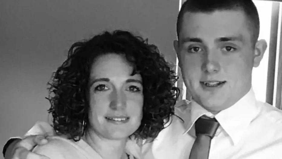 A black and white picture of Rachel Baker, and her son Joe. She has dark curly hair to her shoulders. He has short dark hair and wears a white shirt and dark tie.