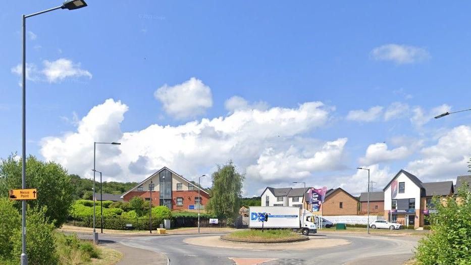 General view of a residential roundabout on a sunny day with a lorry driving round it