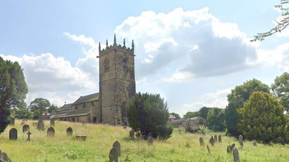 The 10th century St Peter's Church in Felkirk with a traditional view of a grassy churchyard, gravestones, a yew tree and other trees, and a stone wall