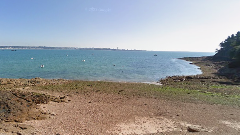 A sandy shoreline and sea water. Boats are in the water. The sky is blue.