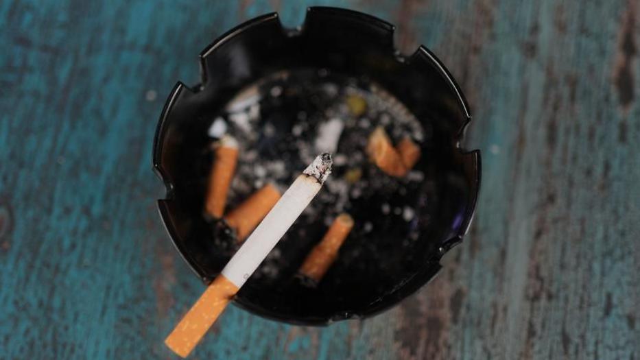 A cigarette is balanced on the edge of a black ash tray.