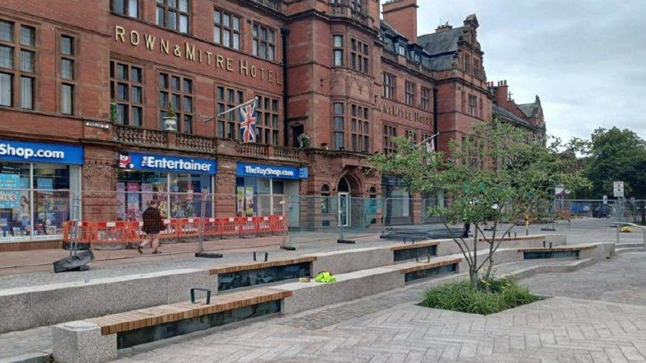 The new seating area, with wooden benches installed on two semi-circular large steps outside the Crown and Mitre hotel, with fencing still in place behind them.