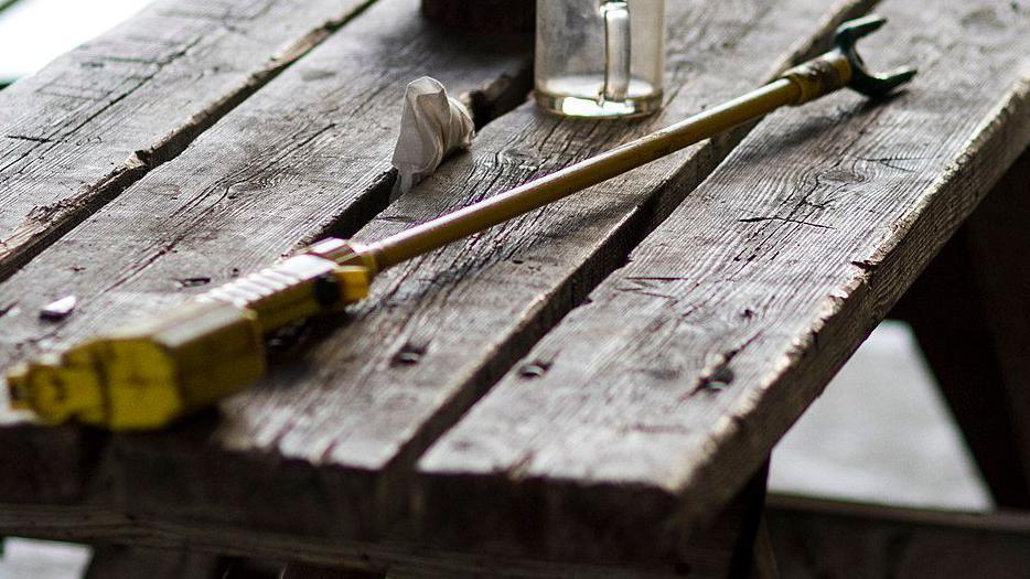 Stock image of an electric cattle prod lying on a wooden bench, with a glass mug in the background