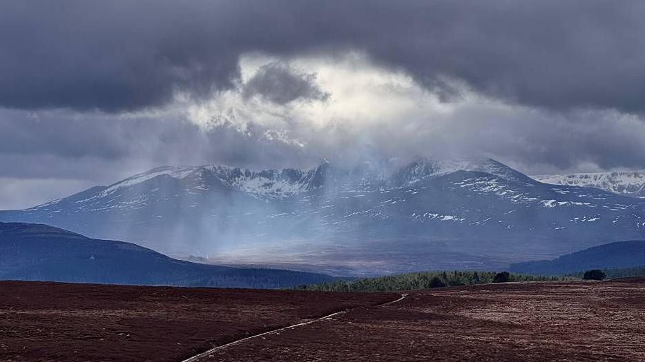 The sun peeking through some grey clouds reflecting down onto some mountain tops.