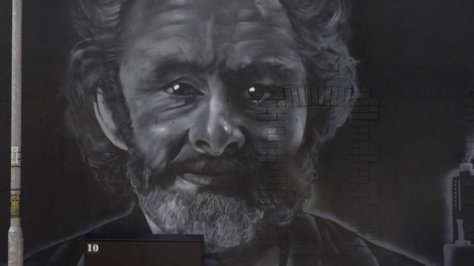 A wall with a black and white painted mural of a man with curly dark hair and a beard.