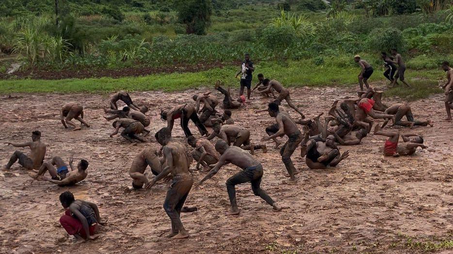 Around 30 men are seen practising forward rolls on a muddy field in Uganda