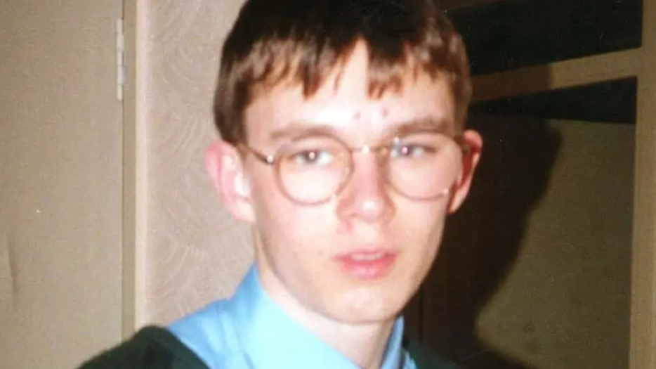 A boy wearing round glasses and a blue shirt looking at the camera.