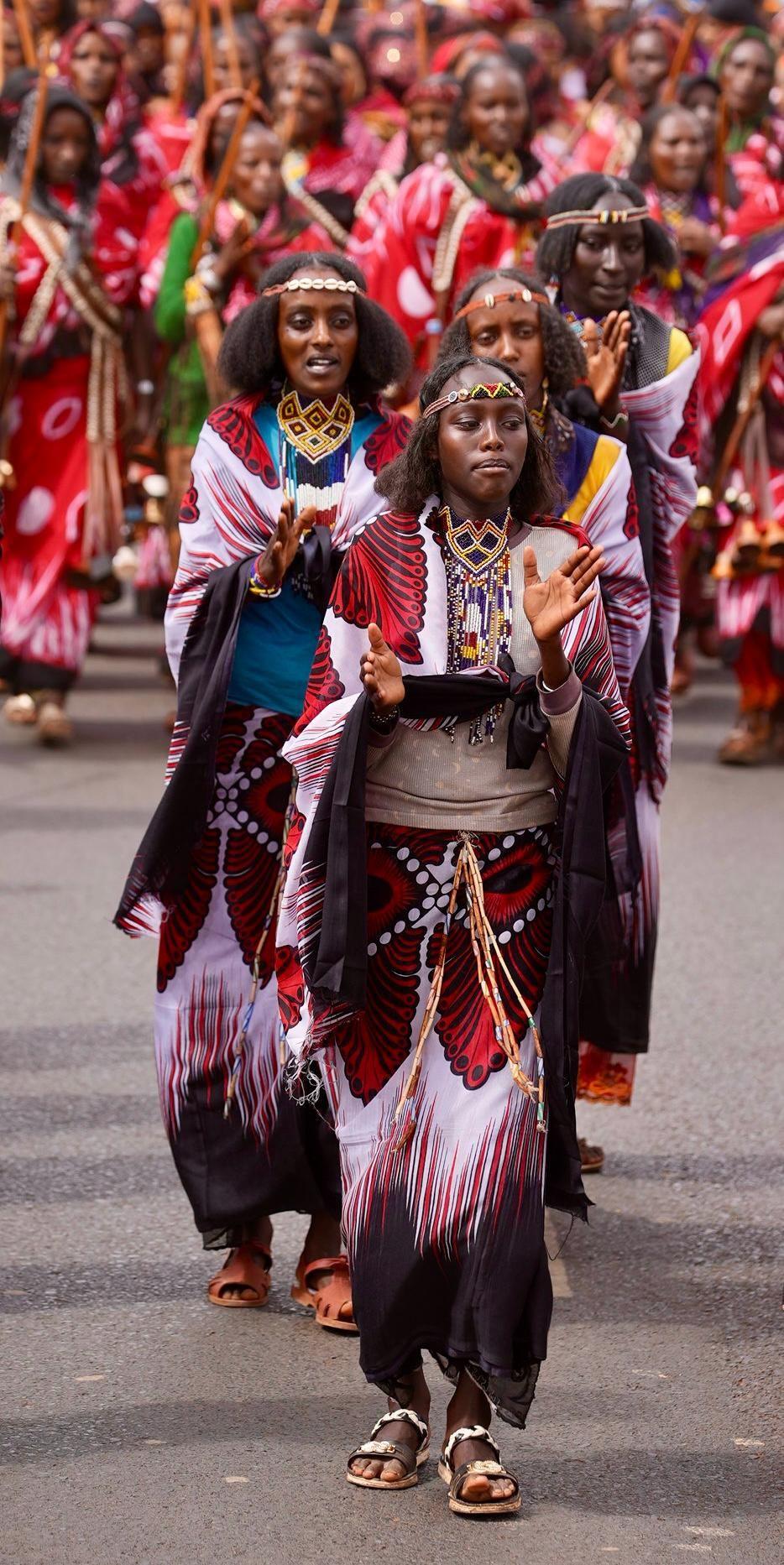 Young women lead the other women. They are dressed in purples and blacks. They do not carry sticks, unlike the married women.