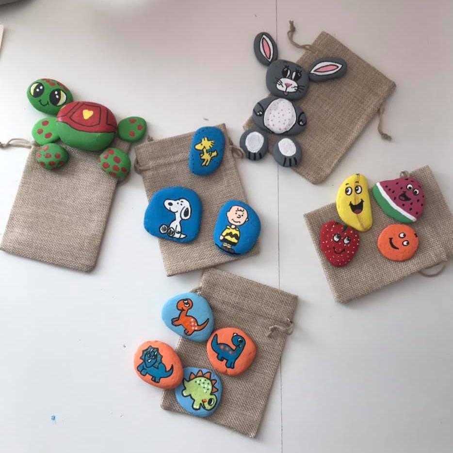 Multiple painted rocks are laid out on a table. On set is painted like a cartoon smiling turtle. Another set of rocks look like various fruits.