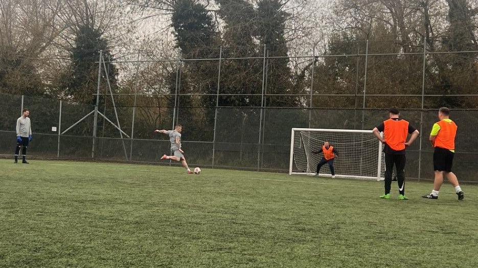 A man takes a football penalty at the homeless league match.