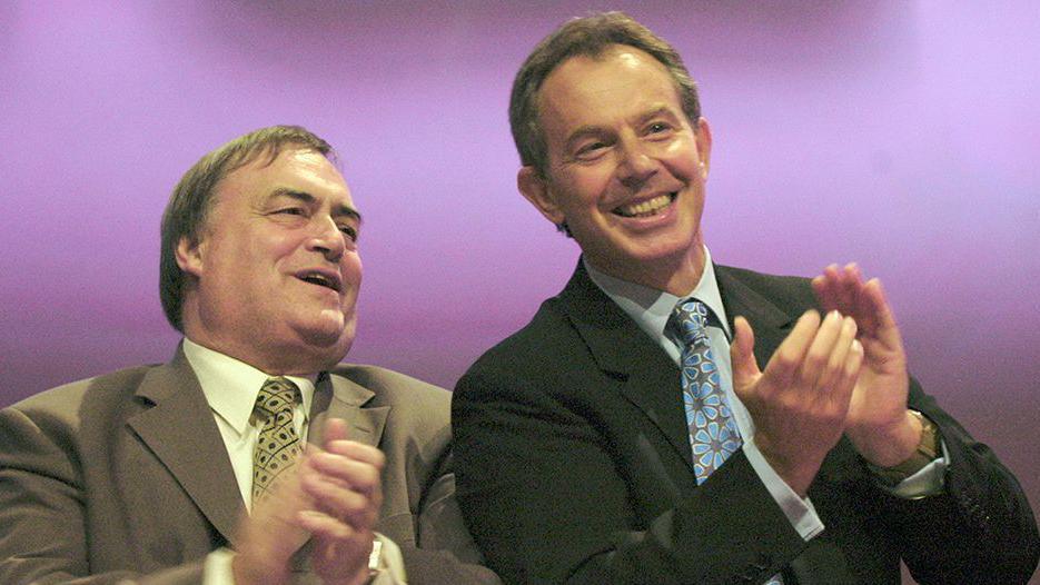 John Prescott pictured with Tony Blair pictured together. Both men are clapping.