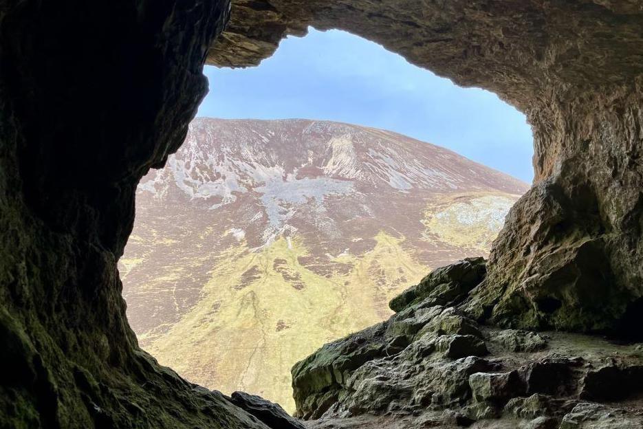 Looking out from a cave towards a steep rocky hillside.