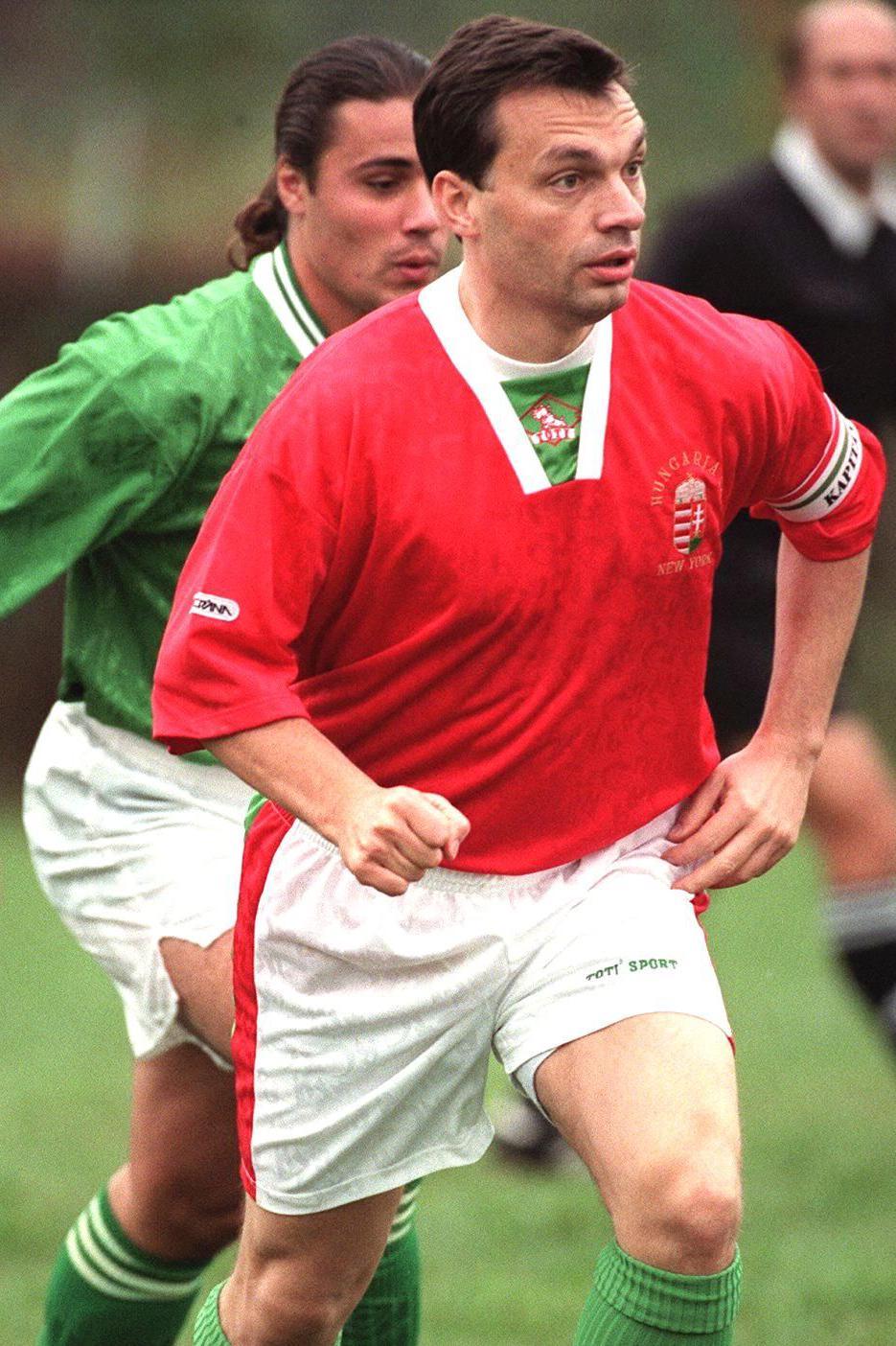 Viktor Orban dressed in a red football kit runs ahead of a green-clad defender