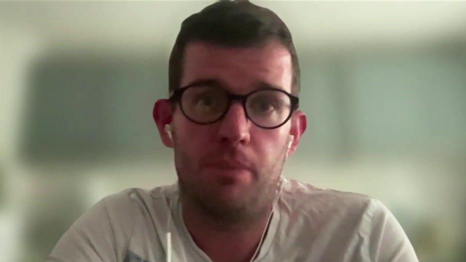 A man with glasses and a white T-shirt stares into the camera. 