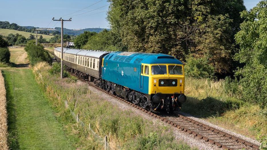 A bright blue and yellow old fashioned train in a shed.