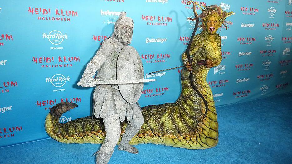 Heidi Klum in a slithering Medusa costume and her husband Tom Kaulitz dressed in gray with a sword and shield, appearing like he was turned to stone.