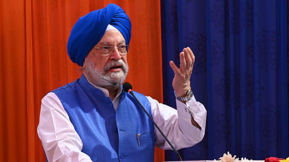 India's federal Minister of Petroleum and Natural Gas Hardeep Singh Puri, wearing blue jacket and turban, with his hand raised, is addressing a gathering.