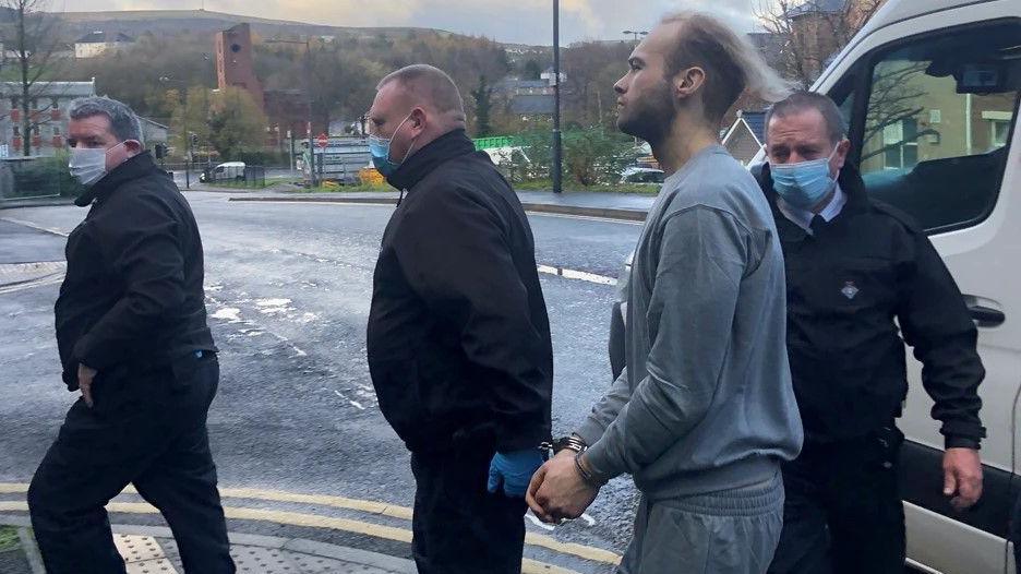 A handcuffed Luke Deeley, wearing a grey tracksuit, is led into court by three security guards