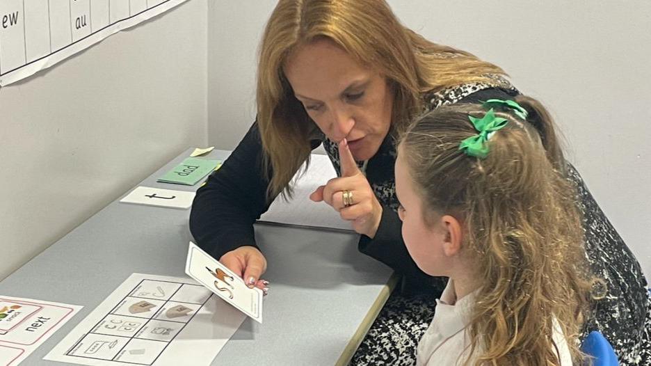 Teacher Samantha Hill holds letter flash cards that a year two girl then identifies and repeats the sound of the letter back to her.