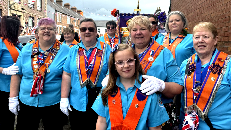 Women of different ages in blue shirts and Orange sashes