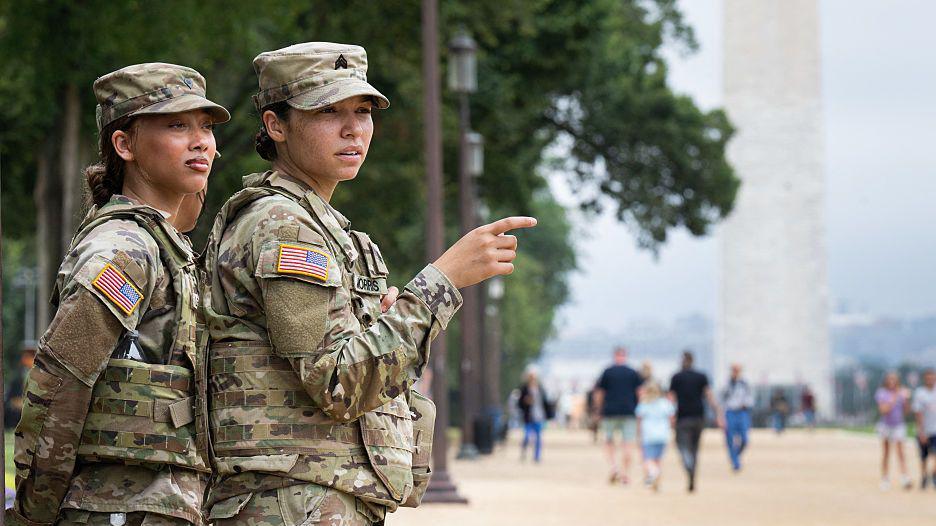 Two female members of the National Guard patrol on the National Mall near the US Capitol in Washington.  They are wearing green camouflage uniforms with the US flag on their right arms.