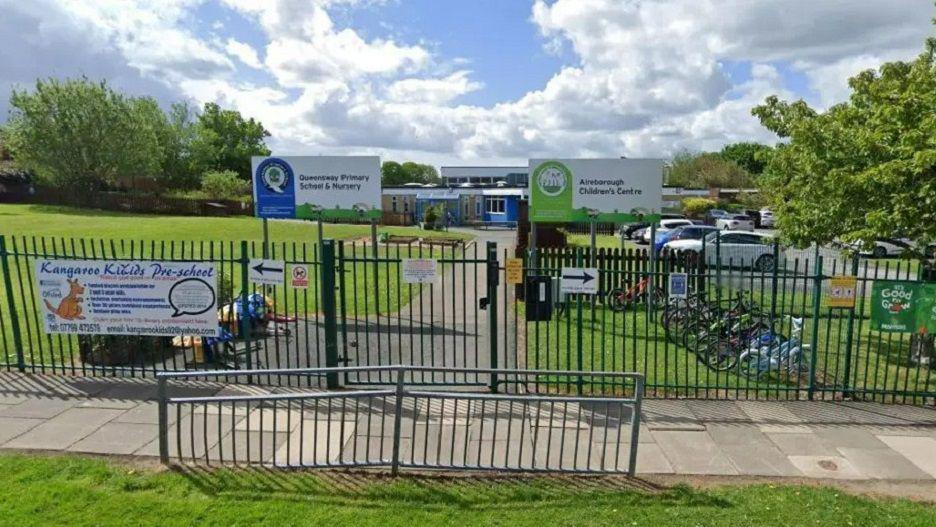 Google Street View image of the outside of the school, with signs and metal fences and grass surrounding it.