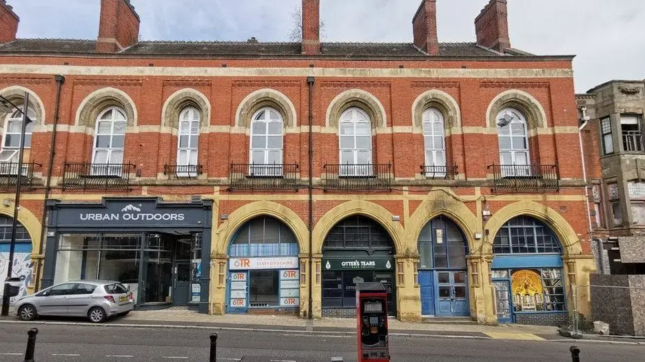 Burslem Market is pictured which is built with bright orange bricks and windows, on a gradient with newer shops underneath it in an arch design.